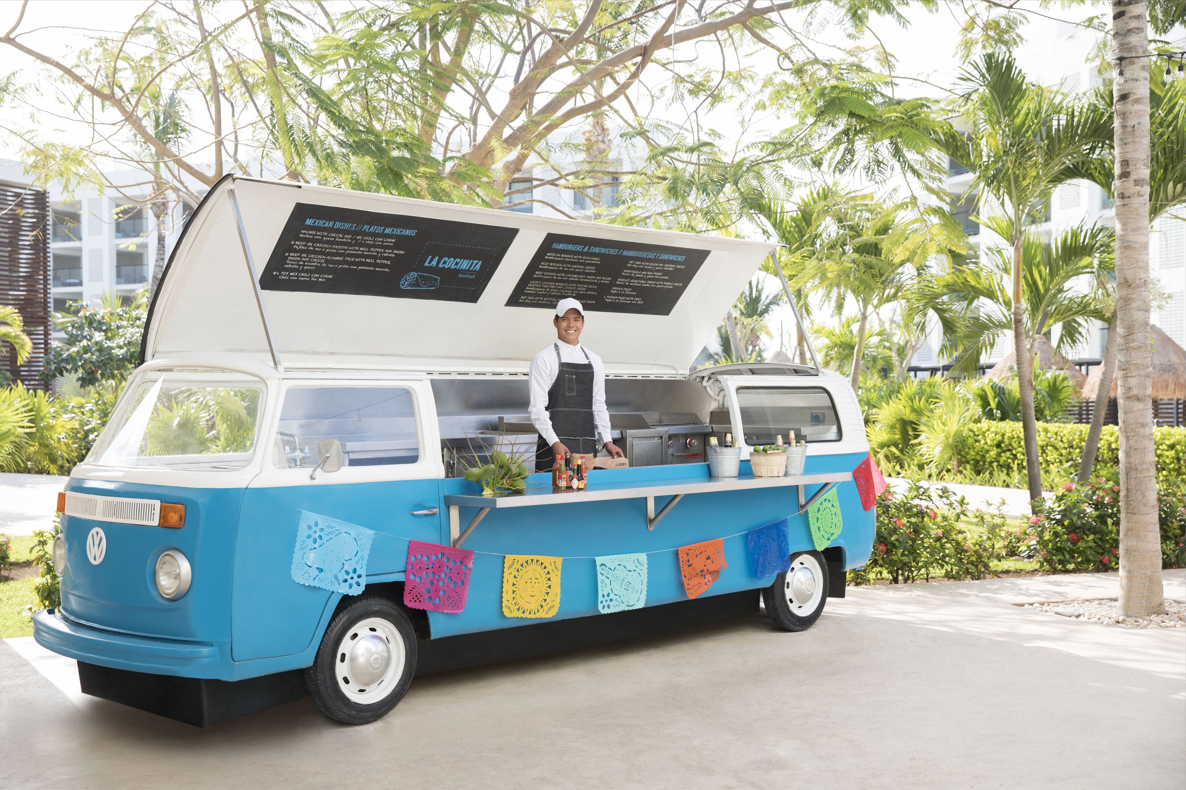A blue and white food truck with a menu board and a person serving.
