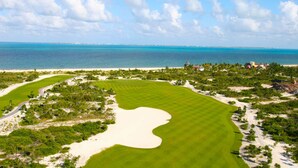A golf course with a large sand bunker, surrounded by greenery and a view of the ocean. - Finest Playa Mujeres by The Excellence Collection - All Inclusive (Punta Sam)