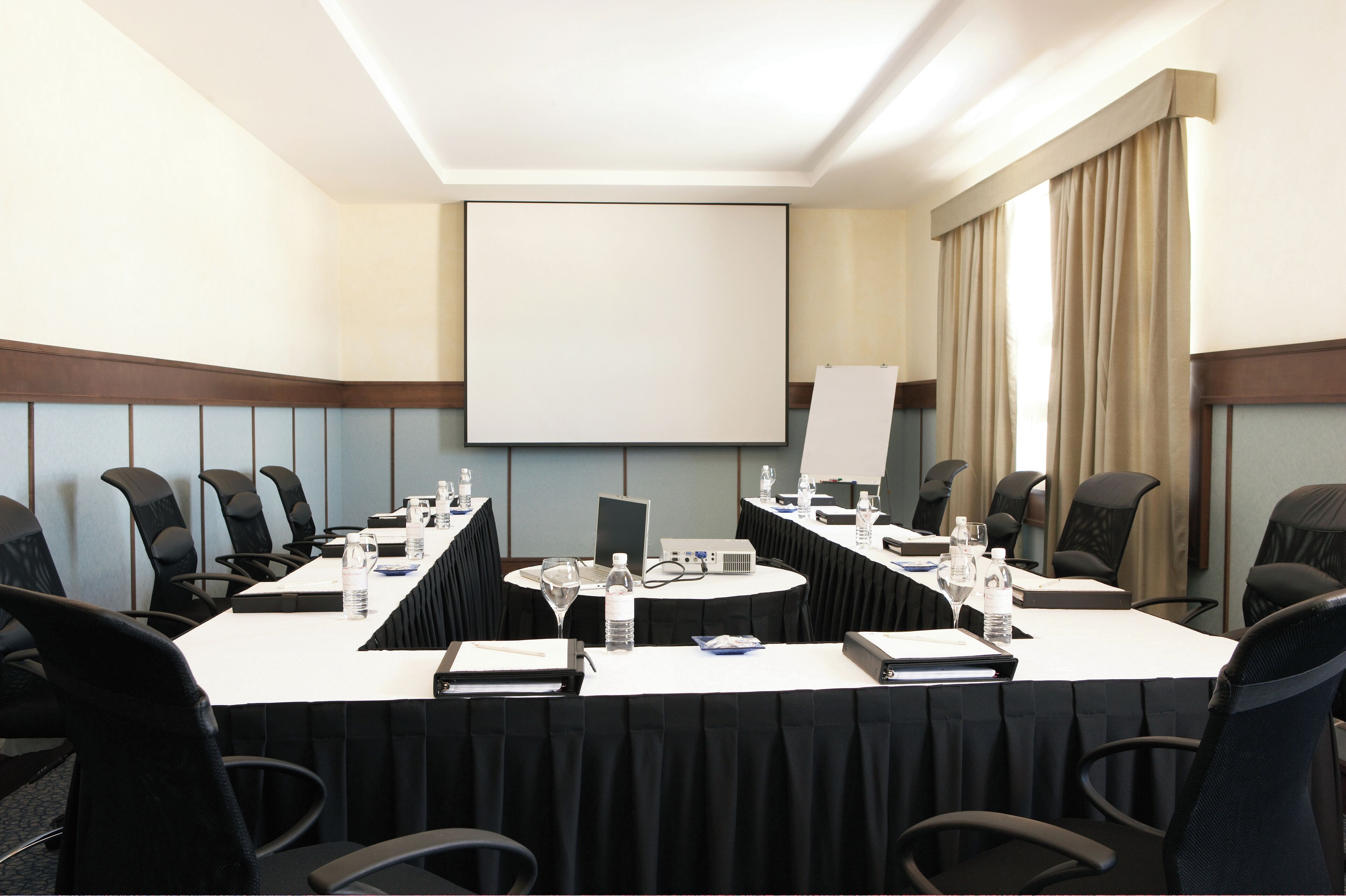 A conference room with a long table, chairs, a projector screen, and a whiteboard.