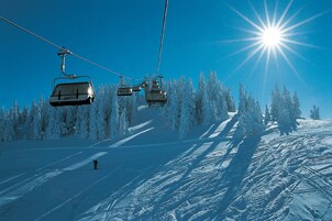 En skilift med stole, der bevæger sig hen over en sneklædt skråning, omgivet af snefyldte træer.