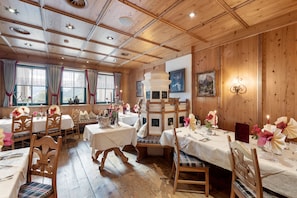 A dining area with wooden paneling, tables set with white tablecloths, and floral centerpieces.
