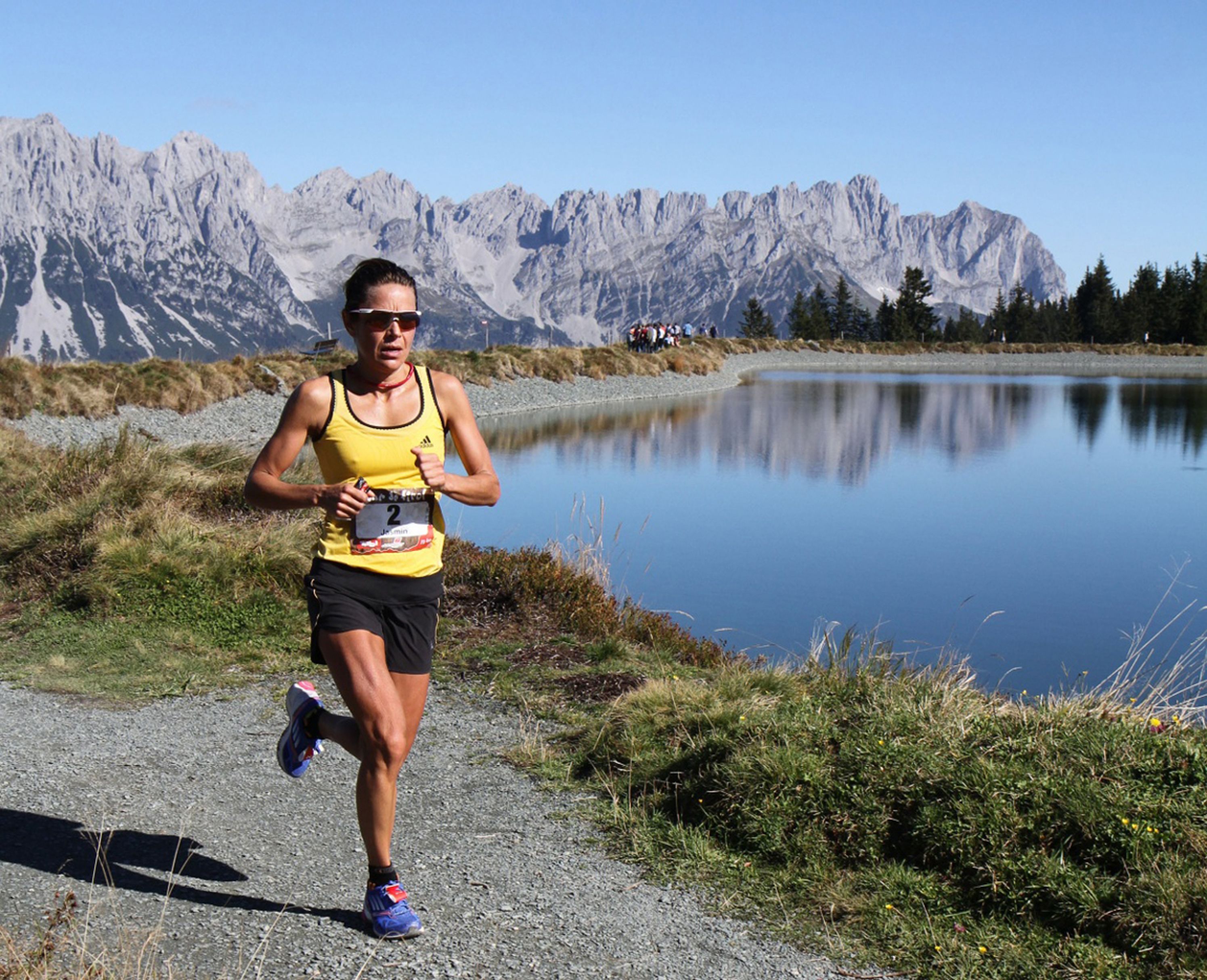 A runner on a gravel path with a lake and mountains in the background.