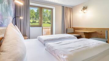 Habitación de hotel con dos camas, un cabecero de madera, una ventana con cortinas y una lámpara fijada a la pared.