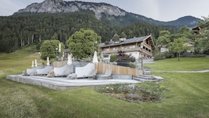 A mountain lodge with a patio area featuring outdoor seating and umbrellas, surrounded by lush greenery and a mountain backdrop. - Landhaus Ager (Soell)