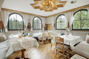 A dining area with multiple tables and chairs, large windows with curtains, and a chandelier. - Landhaus Ager (Soell)