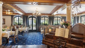 A dining area with tables, chairs, a piano, and large windows with curtains. - Landhaus Ager (Soell)