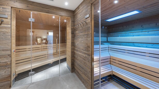 A modern interior with wooden paneling, glass partitions, and a bench area. - Landhaus Ager (Soell)