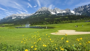 A golf course with a mountain backdrop, a pond, and a fountain. - Landhaus Ager (Soell)