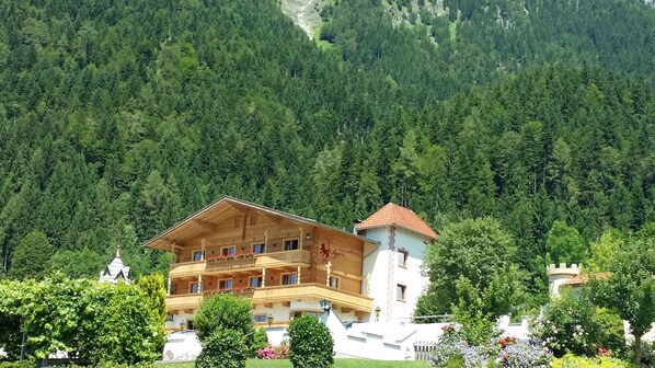 A multi-story wooden building with balconies, surrounded by lush greenery and a forested mountain backdrop. - Landhaus Ager (Soell)