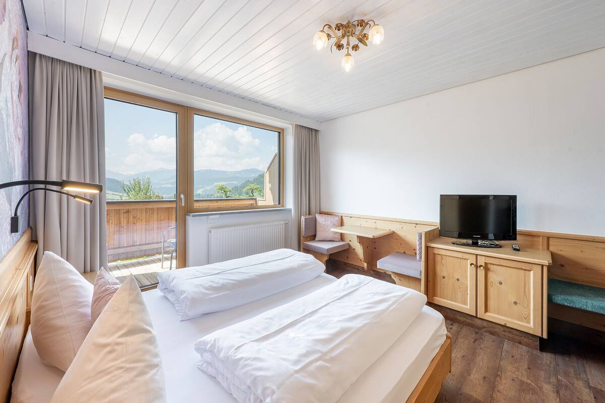 A hotel room with a large bed, a television, a wooden desk, and a view of the mountains.