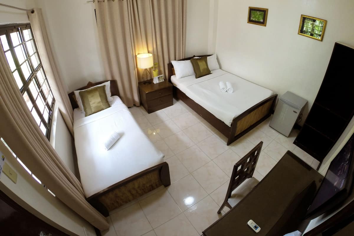 Quarto de hotel com duas camas, uma escrivaninha, uma cadeira, uma mesinha, um abajur e uma televisão.