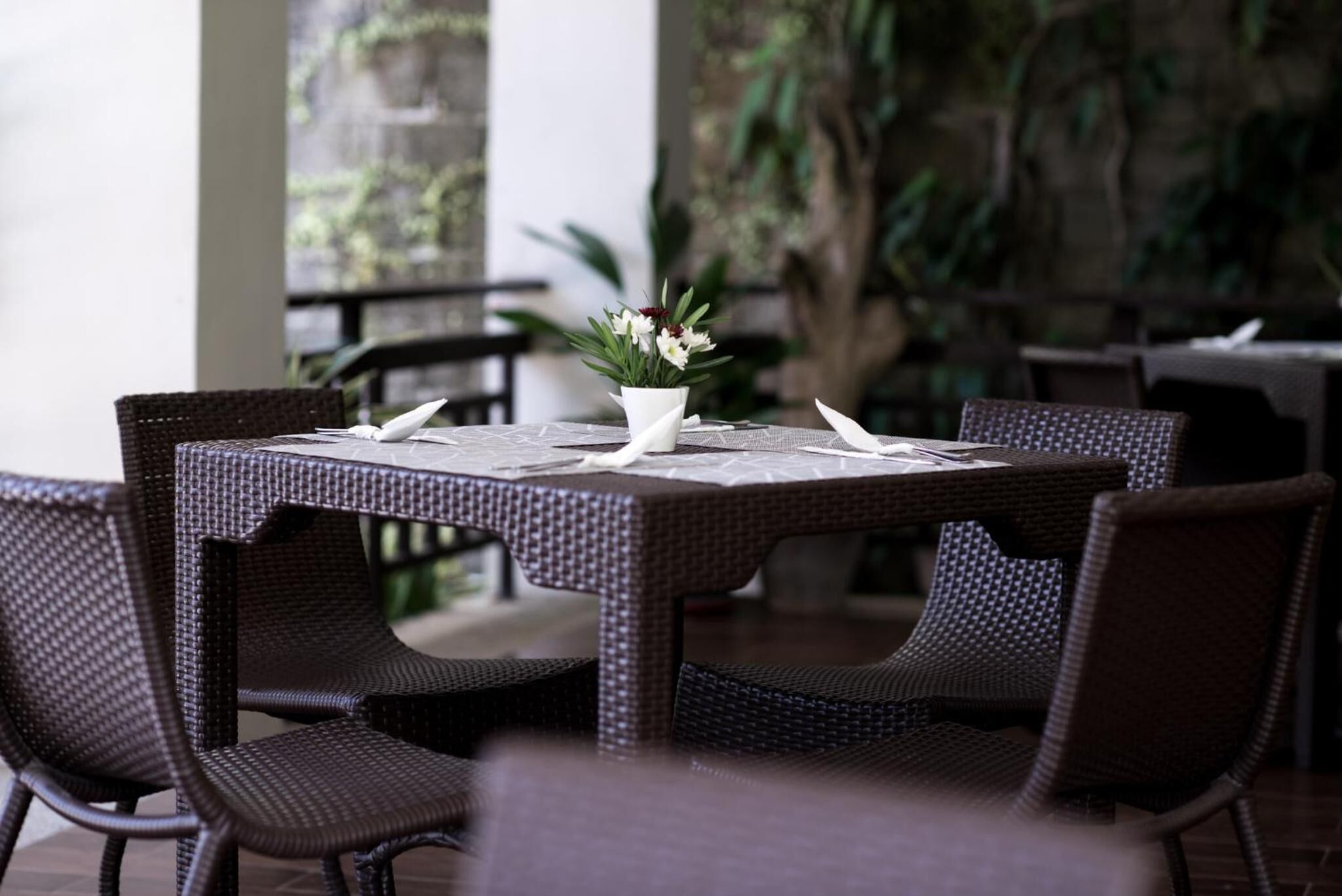 Comedor con mobiliario de mimbre y un jarrón blanco con flores.