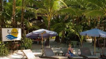 A beachside resort with lounge chairs and umbrellas, palm trees, and a sign for 'Residencia'.
