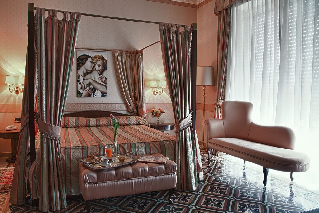 Une chambre à coucher avec un lit à baldaquin, une chaise longue et un sol à motifs.