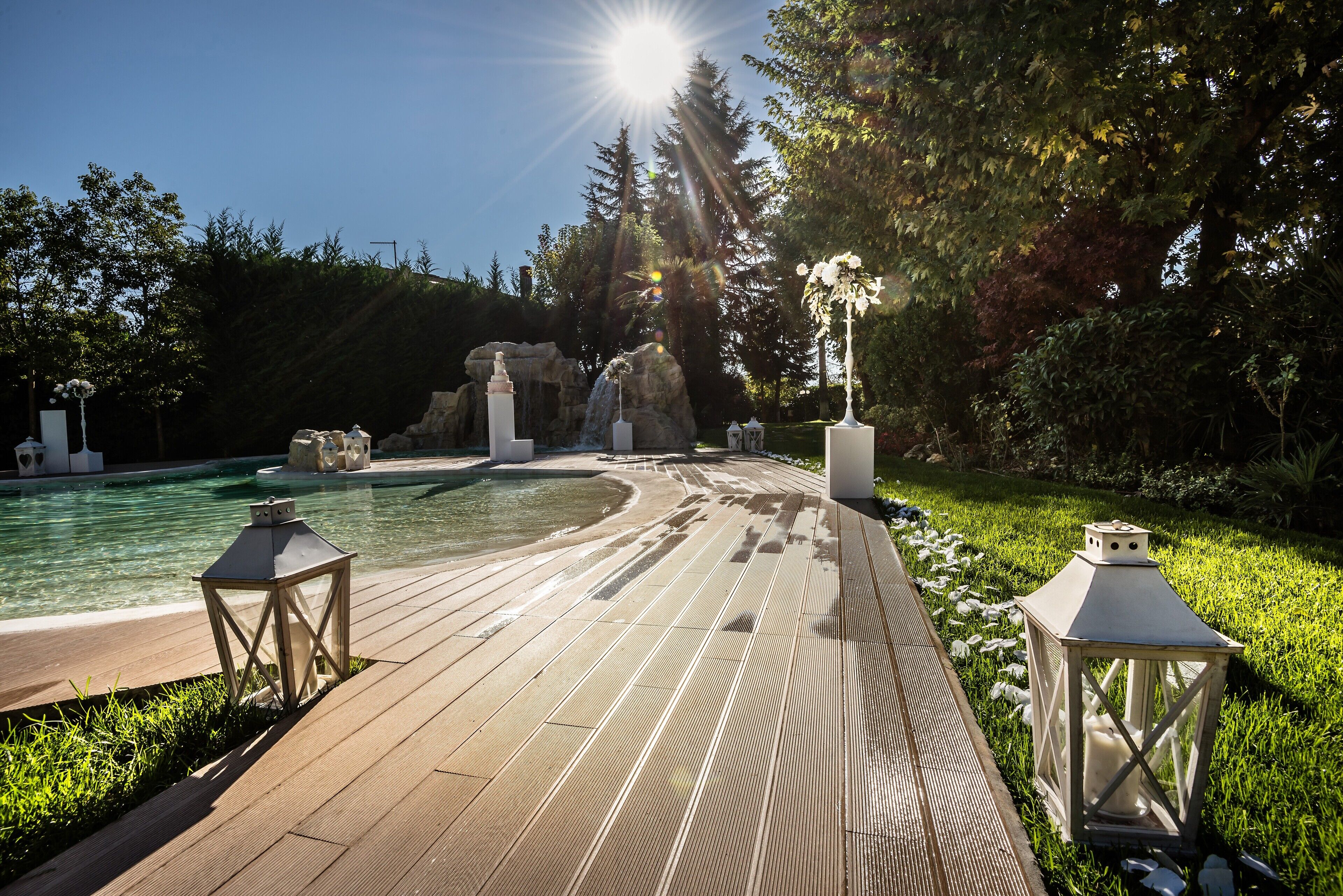 A wooden deck with a pool, surrounded by greenery and decorative lanterns.