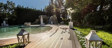 A wooden deck with a pool, surrounded by greenery and decorative lanterns.