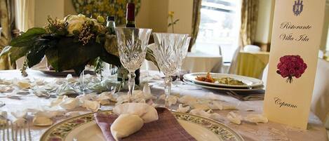 Une table dressée avec des verres en cristal, un centre de table composé de fleurs et un menu.