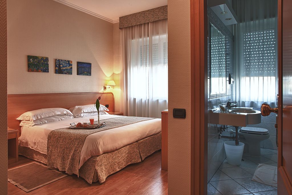 Una habitación de hotel con una cama, una mesita de noche, una lámpara y una ventana con cortinas.