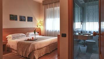Una habitación de hotel con una cama, una mesita de noche, una lámpara y una ventana con cortinas.