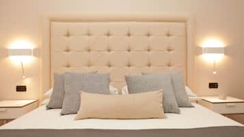 Una cama bien hecha con un cabecero capitonado, varios almohadones y mesitas de noche con lámparas fijadas a la pared.