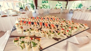 Una mesa de buffet con alimentos ordenados, como sándwiches y ensaladas, en un espacio al aire libre cubierto con carpas.
