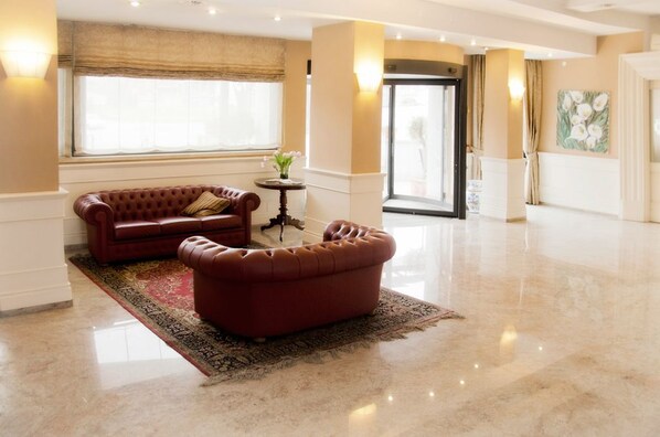 A spacious lobby with a red leather sofa and ottoman, a large window with a view, and a door leading to another area. - Hotel Villa Ida (Ceprano)