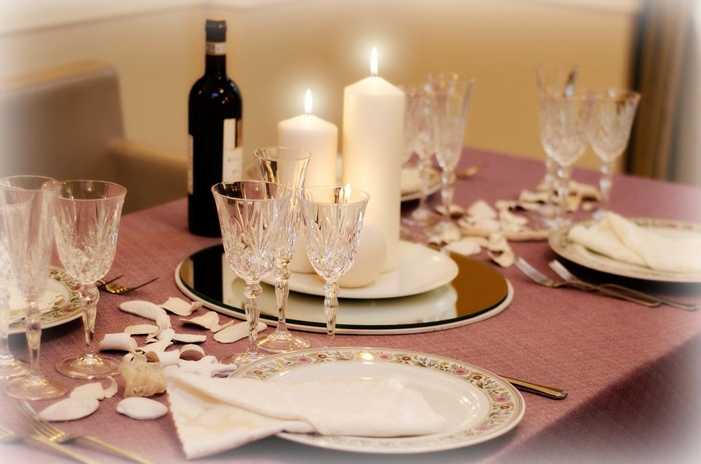 Una mesa lista para una comida, con velas, vino y copas de vidrio transparente.