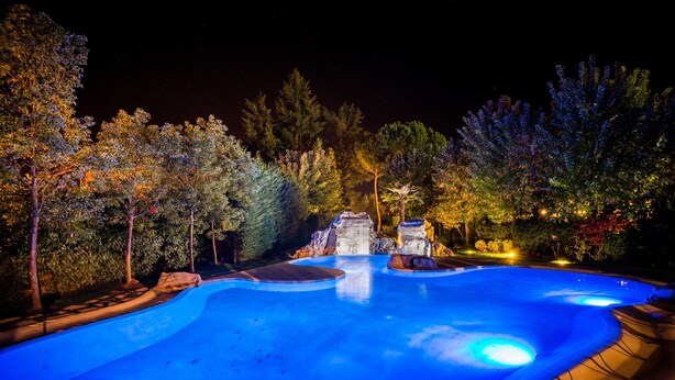 Una piscina con una cascada, rodeada de árboles e iluminada con luces azules.