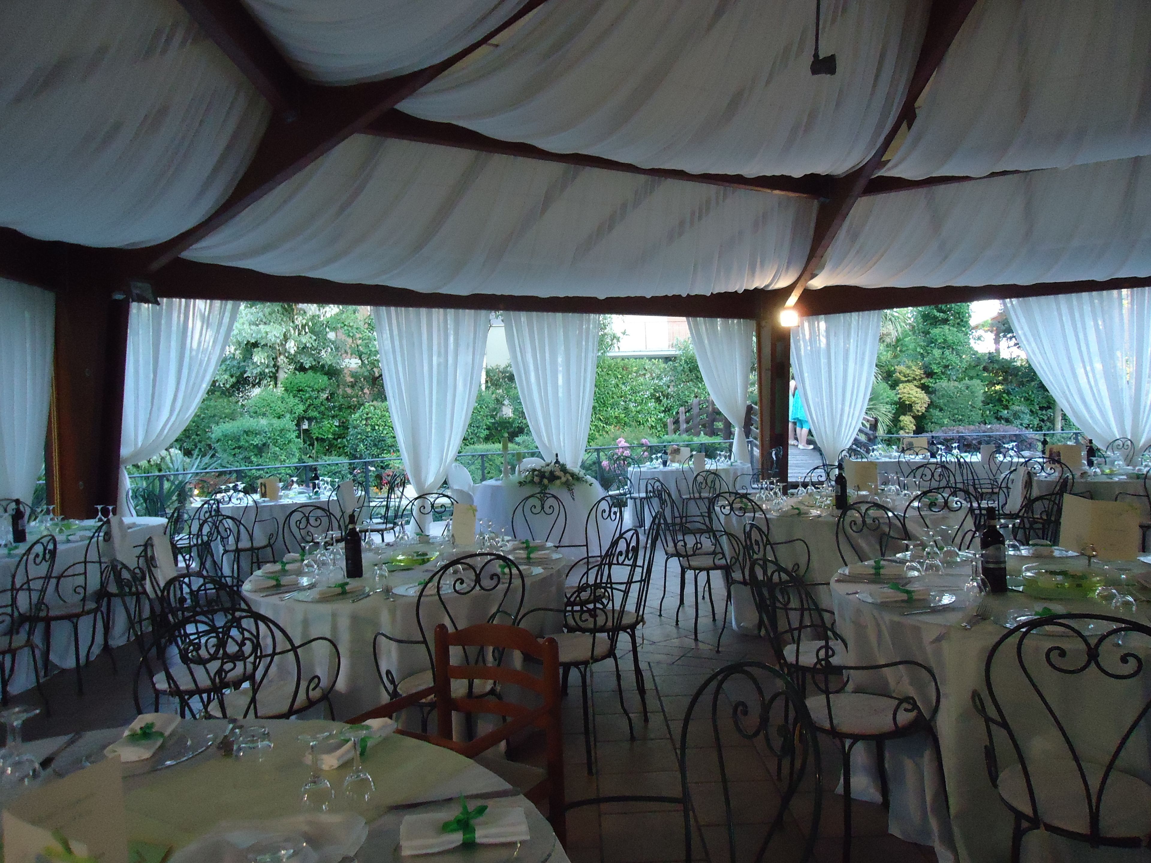 An outdoor dining area with round tables, metal chairs, and white tablecloths.