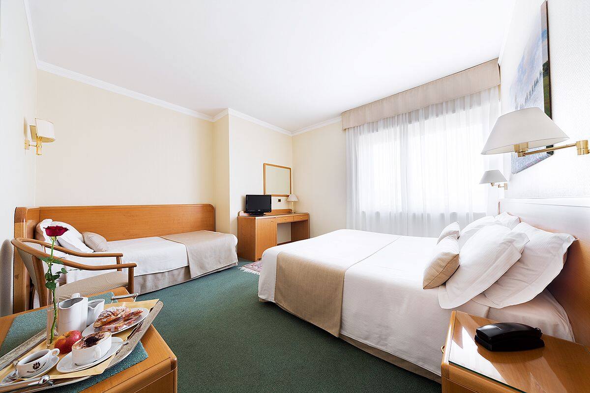 Une chambre d’hôtel avec deux lits, un bureau, une chaise et un coin repas où le petit-déjeuner est servi.