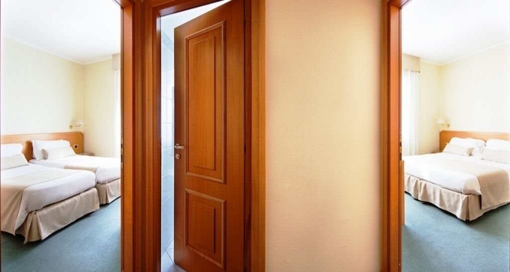 Una habitación de hotel con dos camas, una puerta de madera y una alfombra de color claro.