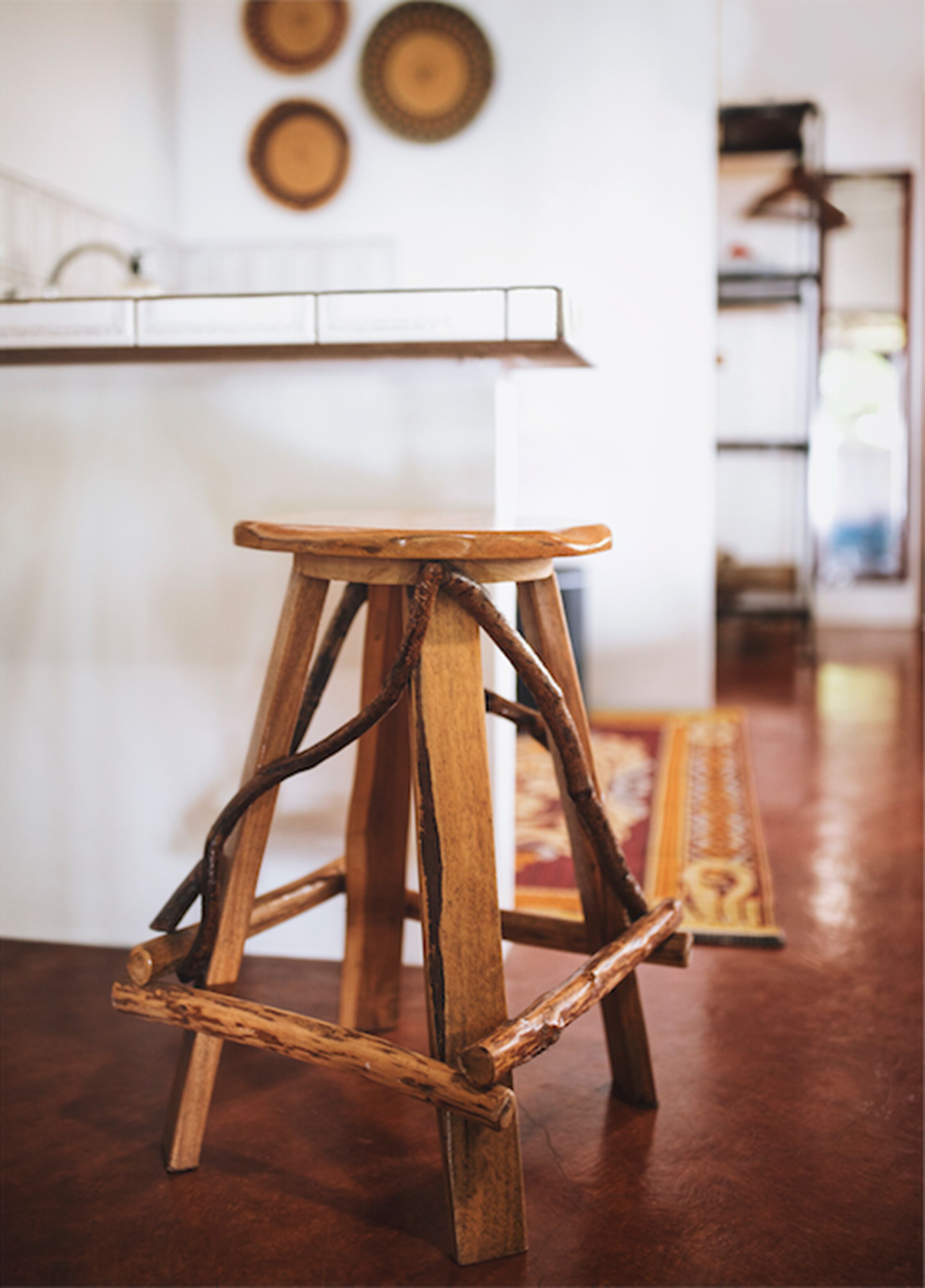 Un taburete de madera rústica con un diseño original, colocado en una habitación luminosa con salpicadero de azulejos y suelo de madera.