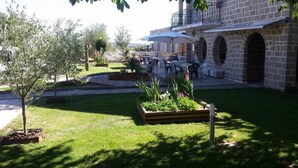 Un área de estar al aire libre con mesas y sombrillas, rodeada de edificios de piedra y vegetación.