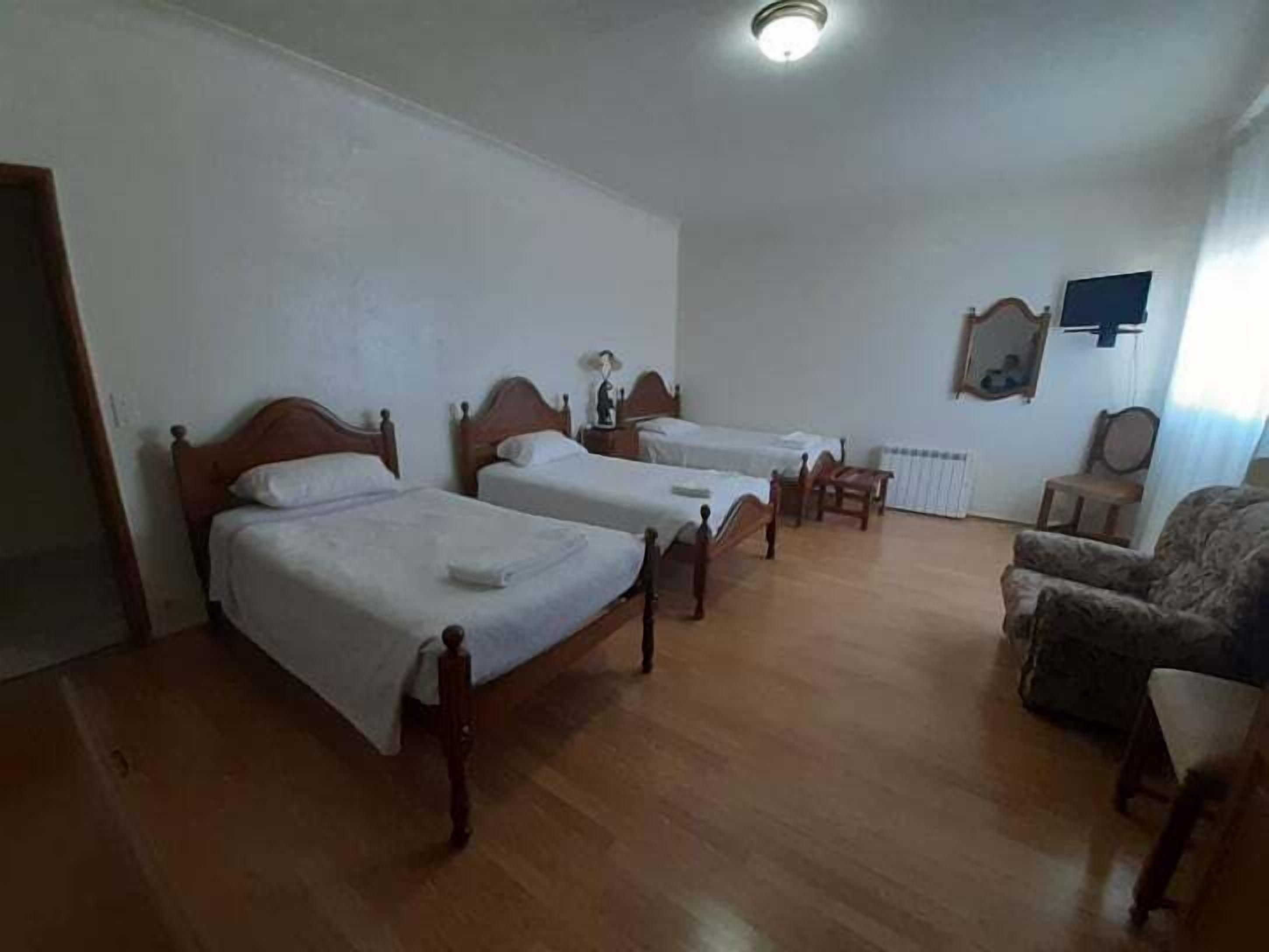 A room with two wooden beds, a wooden chair, a small table, and a radiator.