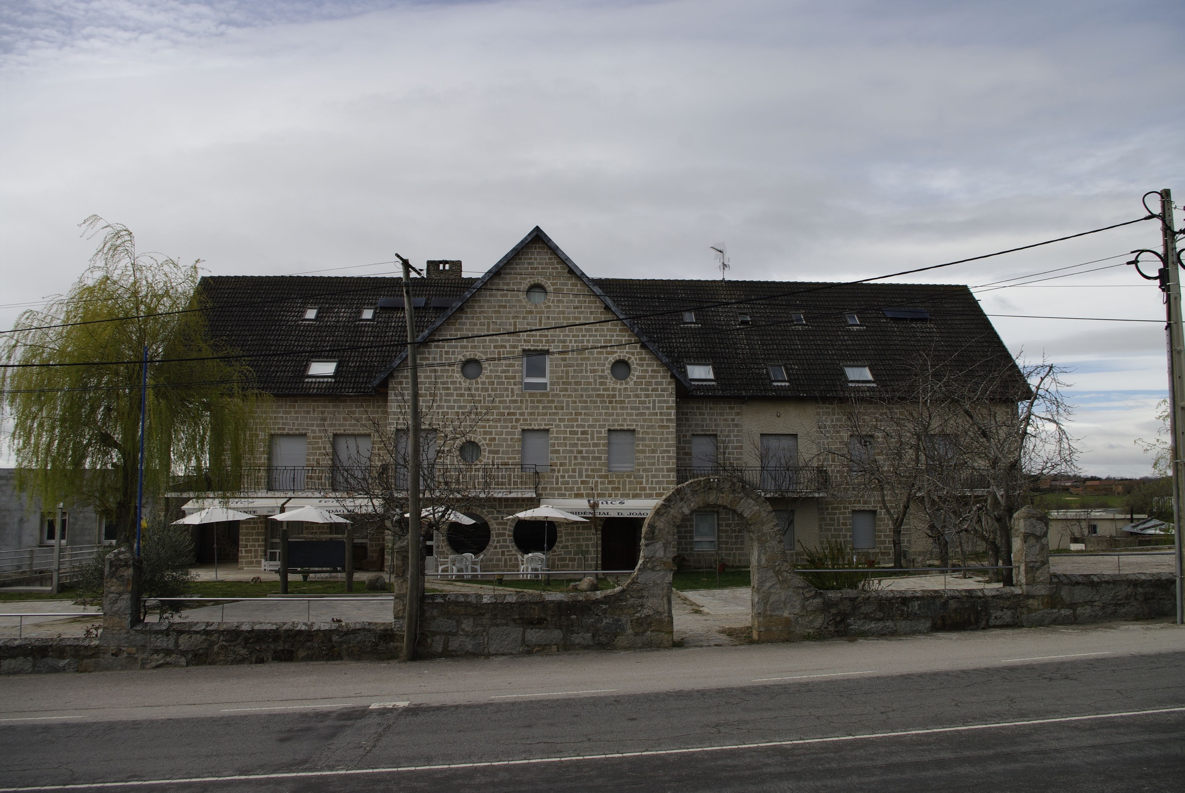 A stone building with a sloped roof, multiple windows, and outdoor seating with umbrellas.
