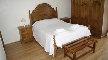 Una cama bien hecha con cabecera de madera, una mesita de noche de madera con lámpara y un banco de madera.