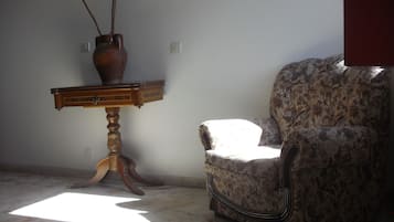 A room with a wooden side table, a floral armchair, and a vase with branches.