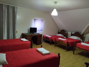 Een kamer met drie bedden, een bureau met een computer en een raam met gordijnen.