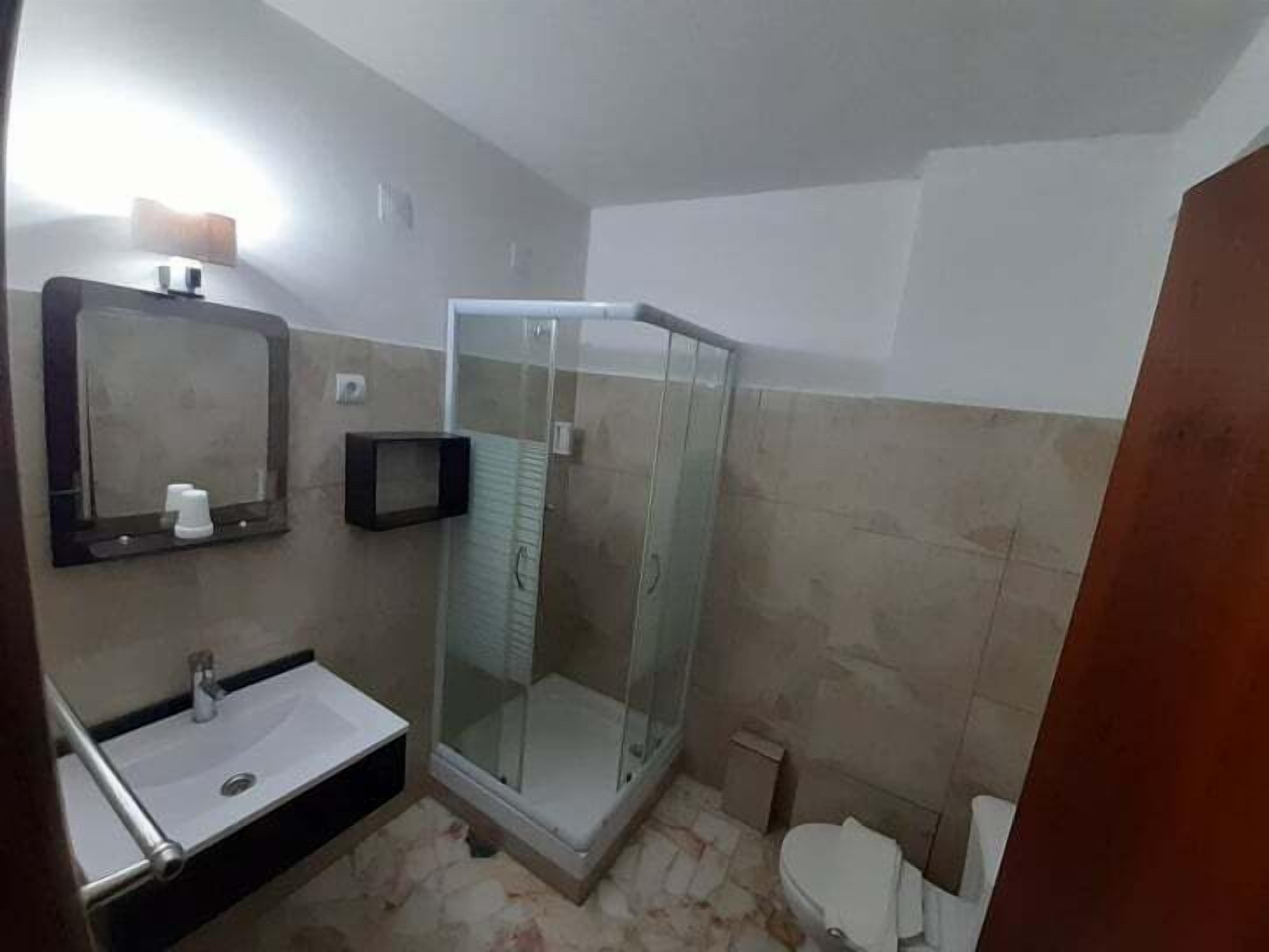 Casa de banho com cabine de chuveiro envidraçada, lavatório com espelho e sanita.
