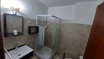 Casa de banho com cabine de chuveiro envidraçada, lavatório com espelho e sanita.