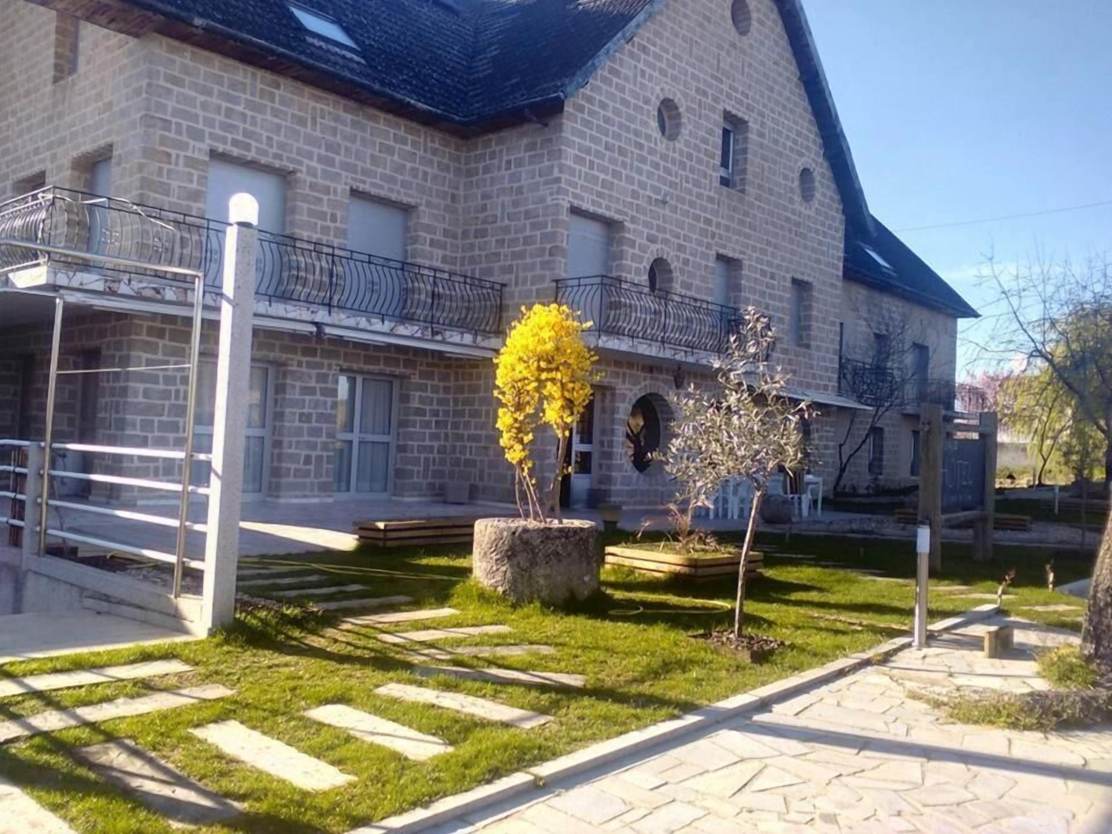Un bâtiment en pierre doté d’un balcon, un petit jardin avec des fleurs jaunes et un chemin pavé.