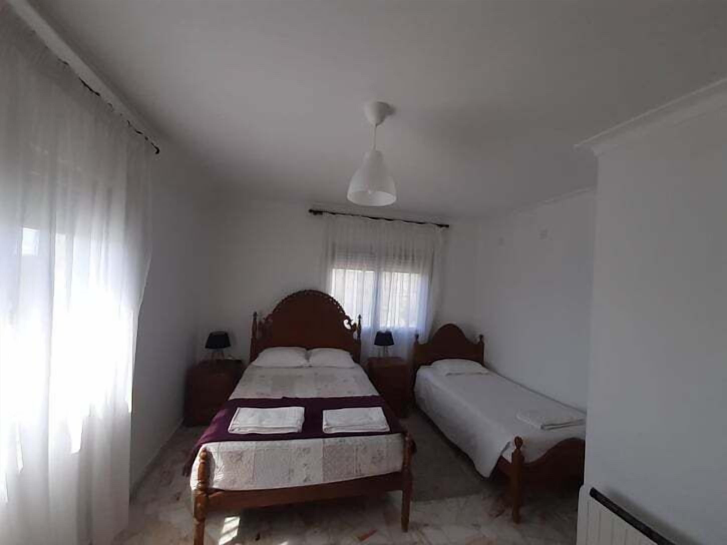 Een slaapkamer met een enkel bed, een kleiner bed, een nachtkastje, een lamp en een plafondventilator.