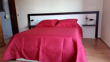 A bed with a red quilted cover, a wooden headboard, and a bedside table with a lamp.