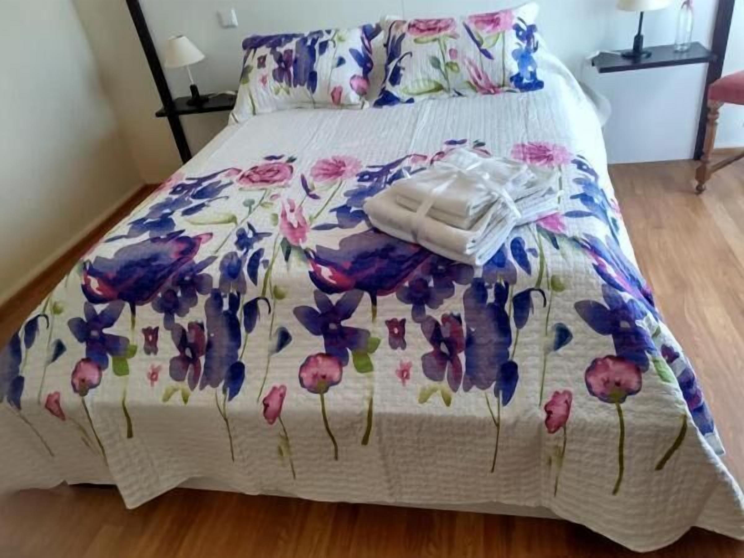 Uma cama com colcha florida, travesseiros e uma toalha dobrada.