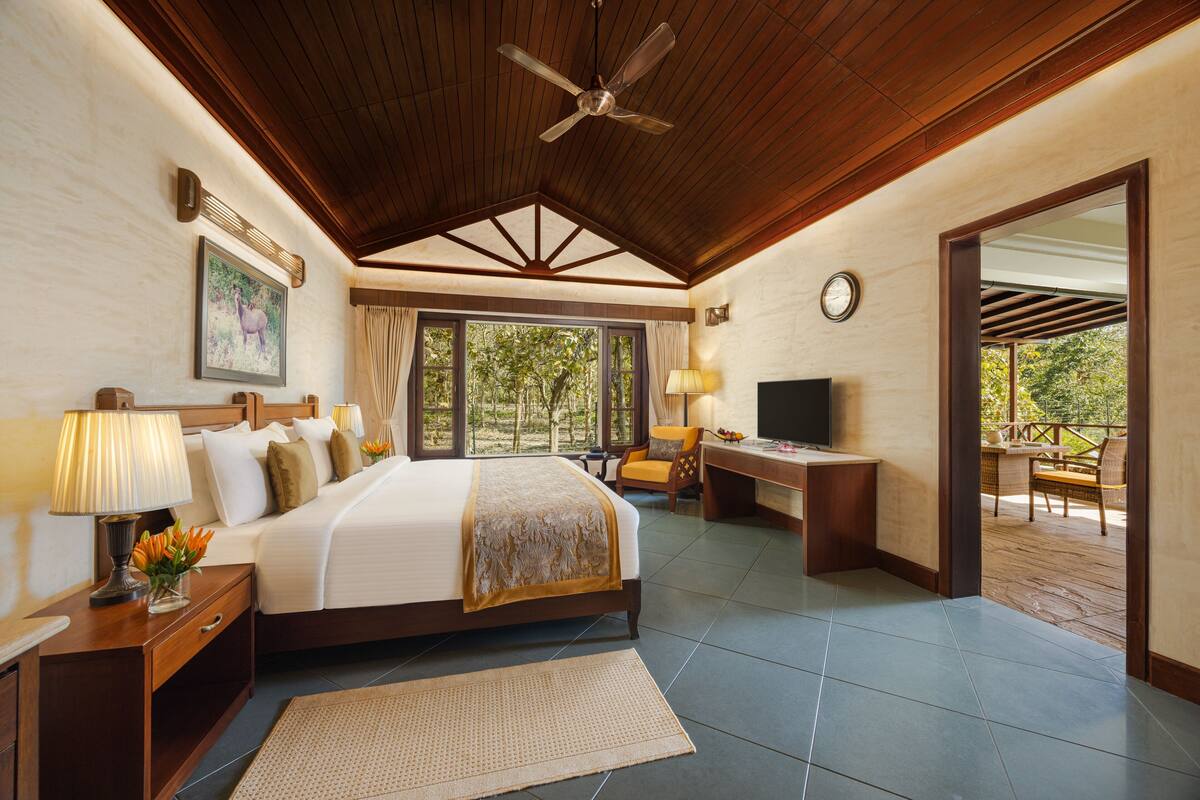A spacious bedroom with a large bed, a desk, a television, and a view of the outdoors.