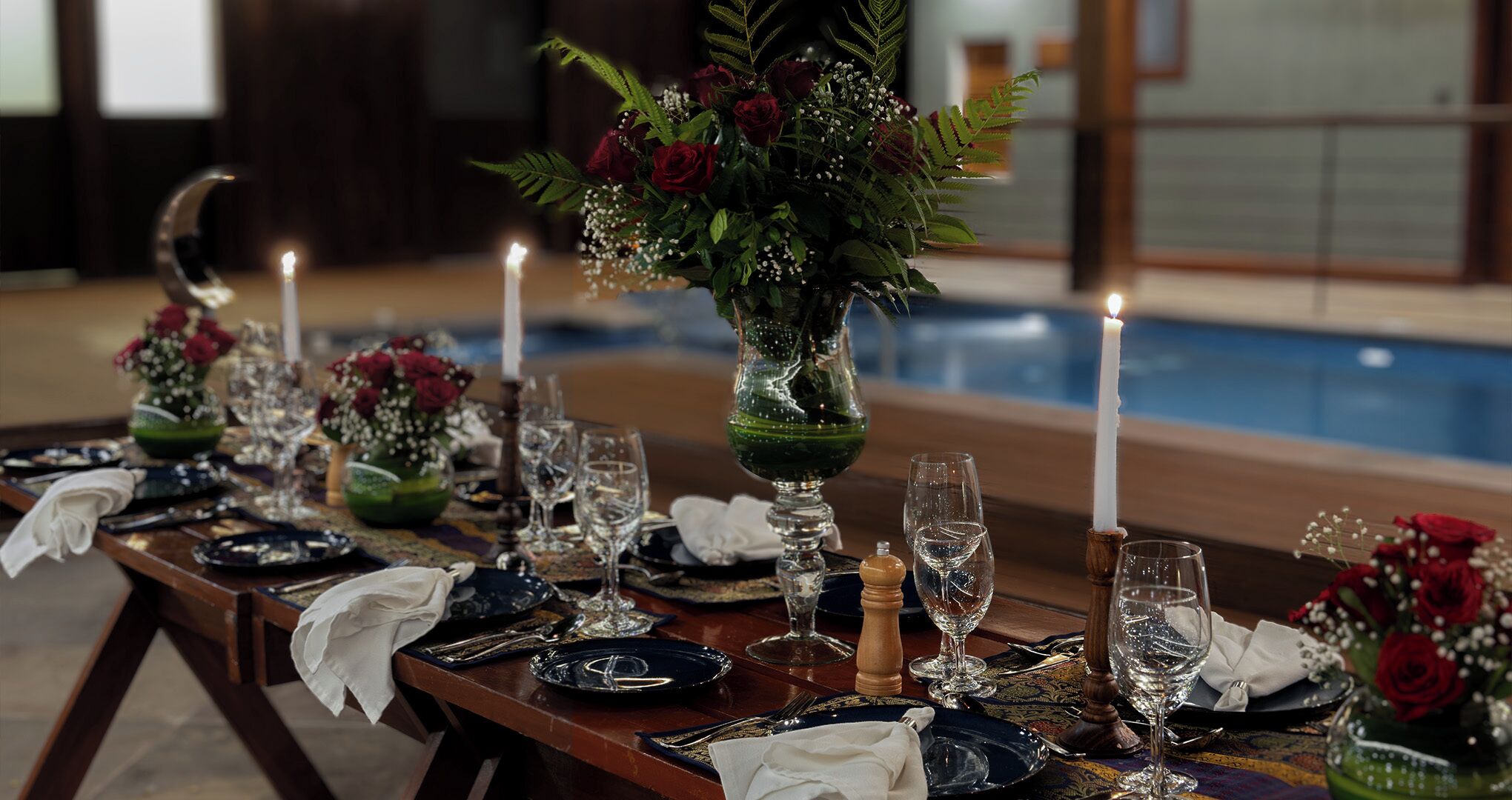 A dining table set with plates, glasses, and candles, with a pool visible in the background.