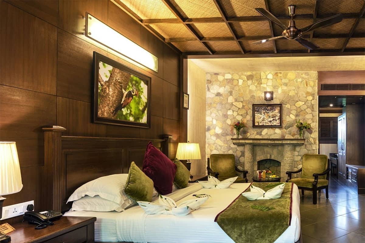 A hotel room with a bed, a nightstand, a telephone, a lamp, a fireplace, and a stone wall.
