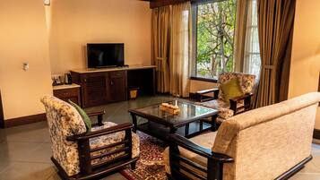 A living room with a sofa, armchairs, a coffee table, a television, and a window with curtains.