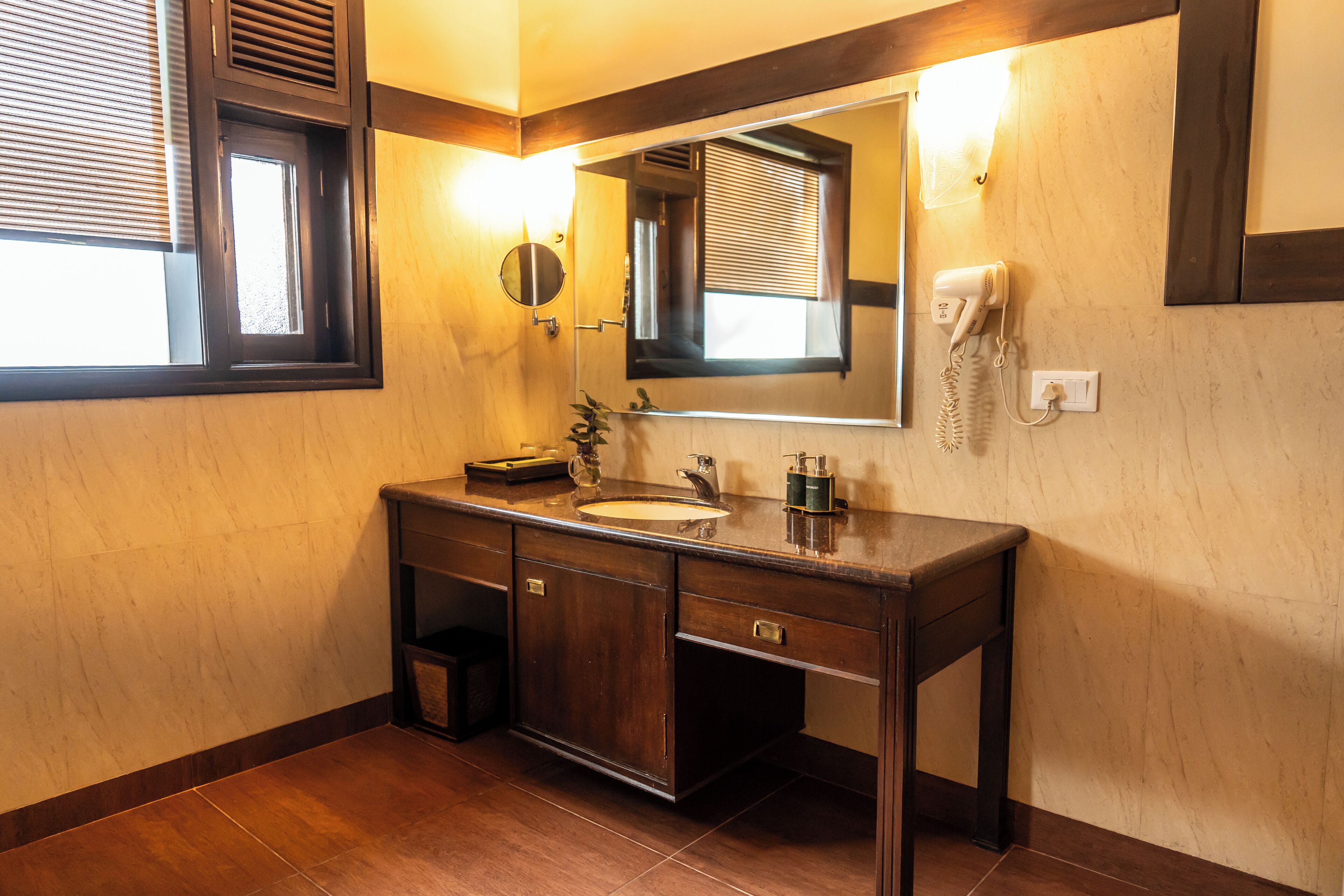 A bathroom with a wooden vanity, a mirror, a sink, and a hairdryer mounted on the wall.
