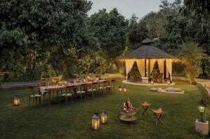 Un área de comedor al aire libre con un pabellón de techo de paja, rodeado de exuberante follaje.